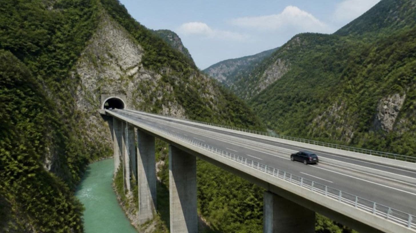 Un'autostrada moderna con viadotti e gallerie tra montagne verdi