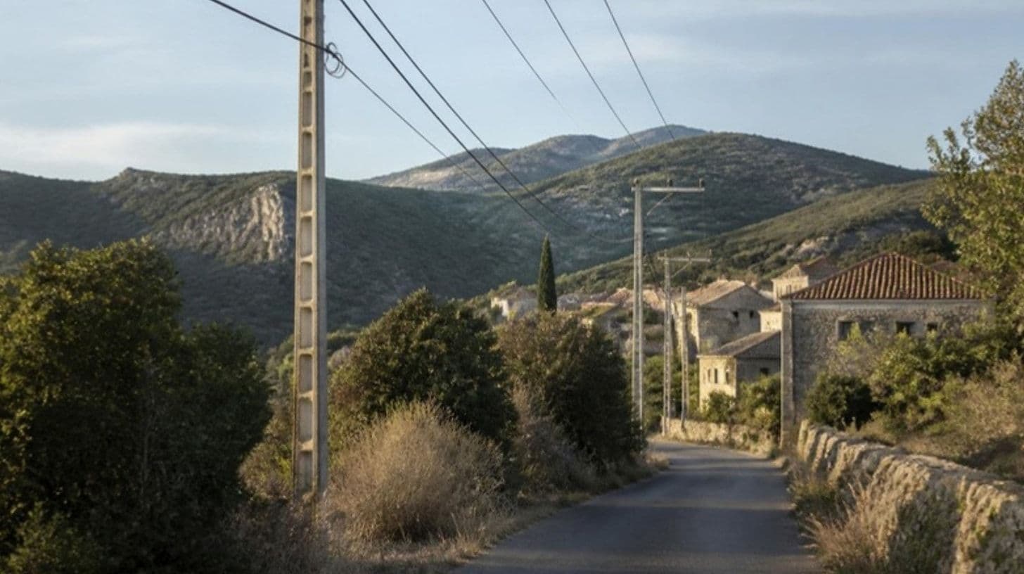 Stromleitungen an Betonmasten entlang einer Landstraße mit Steinhäusern