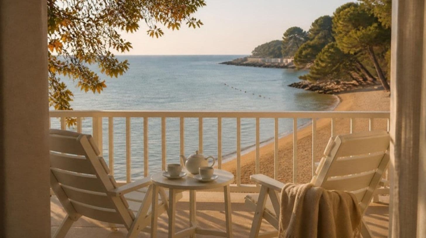 Ein Hotelbalkon am Meer im Frühherbst mit zwei leeren Liegestühlen, einer Teekanne und einer Decke