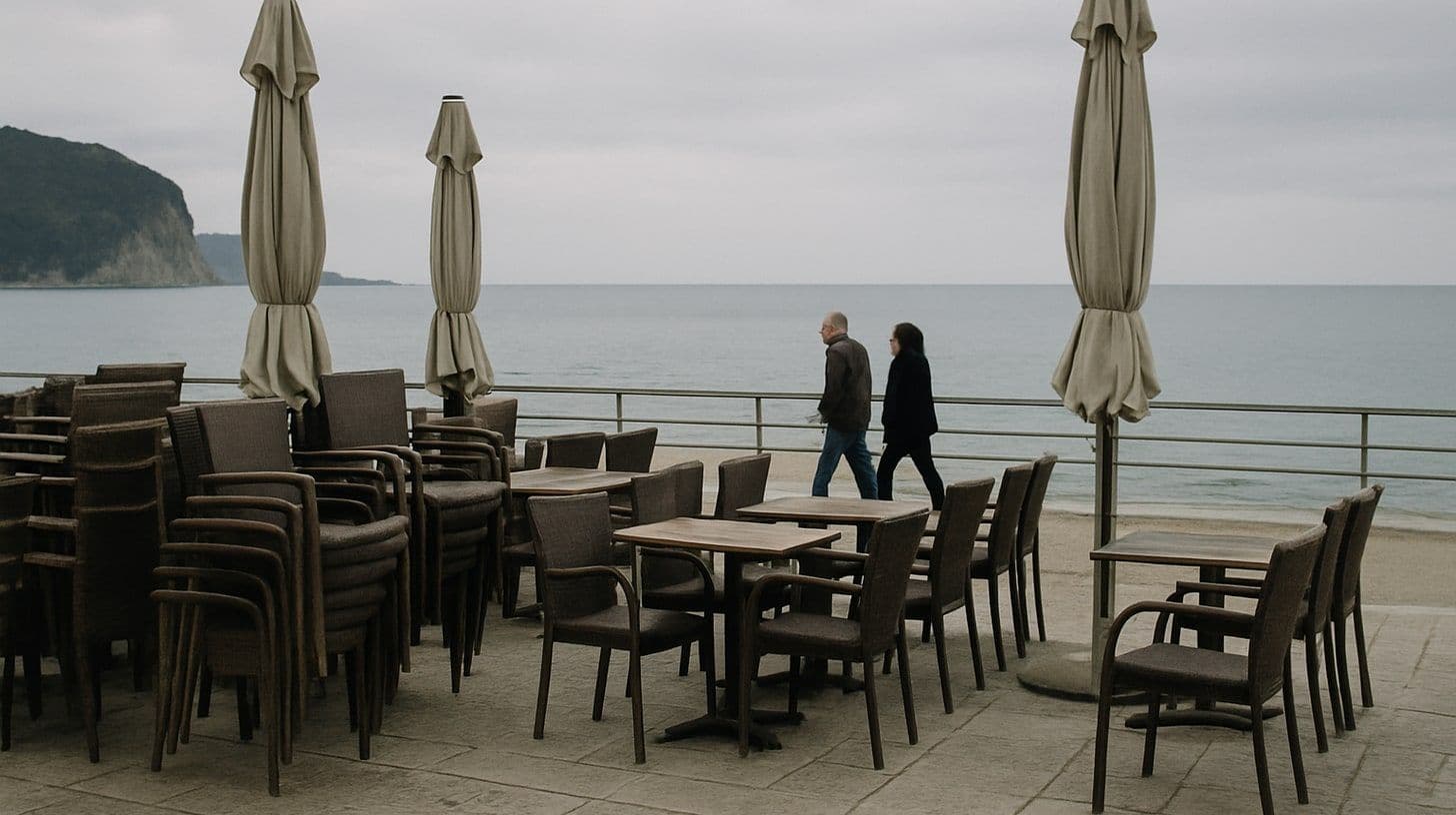 An empty cafe terrace on the Budva seafront in November, chairs stacked, a calm sea behind