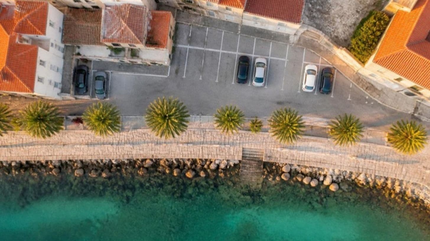 An aerial view of street parking by a promenade with palm trees and turquoise sea