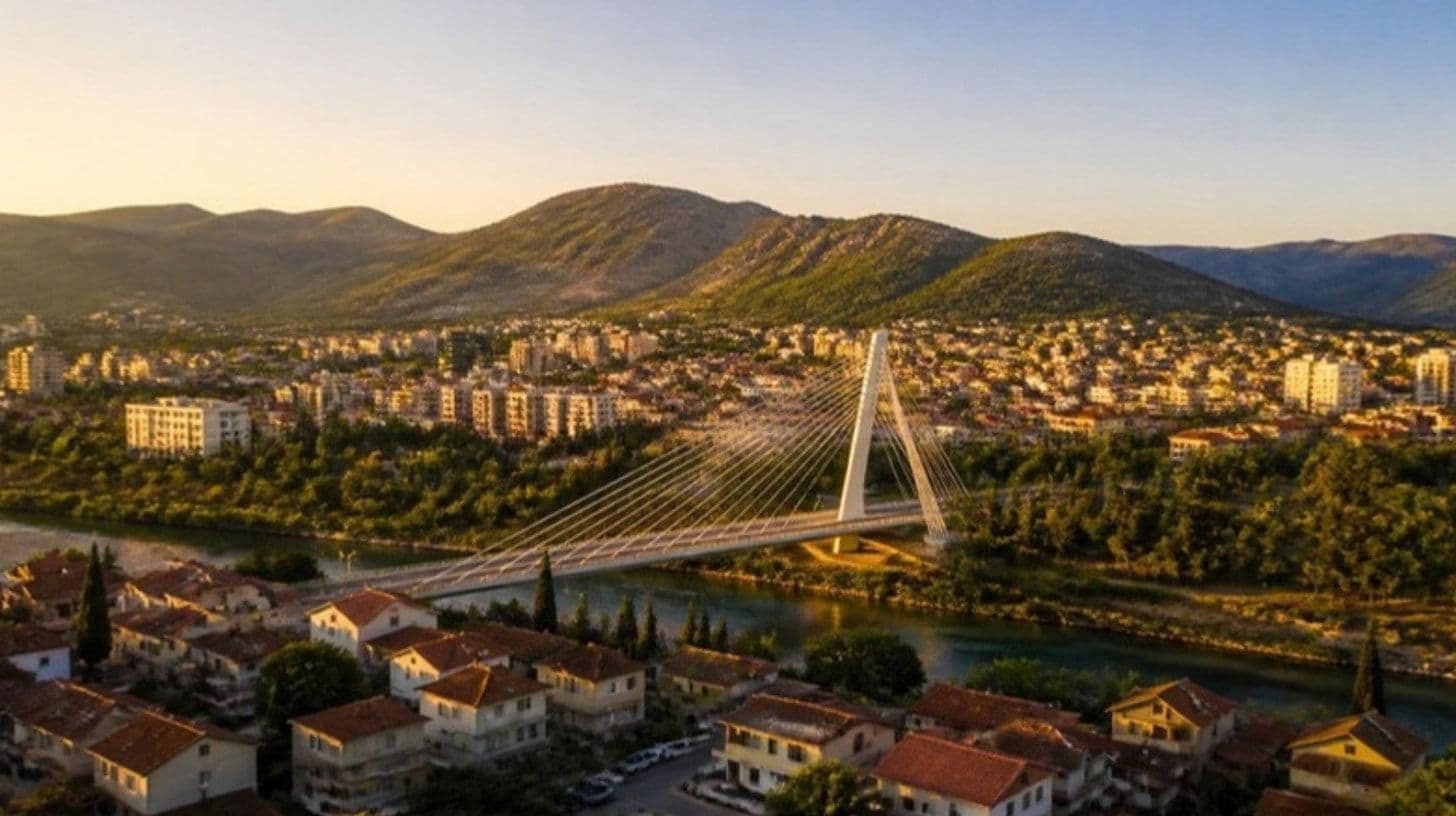 Vista di una piccola città moderna lungo un fiume con un ponte bianco e colline sullo sfondo all'ora d'oro